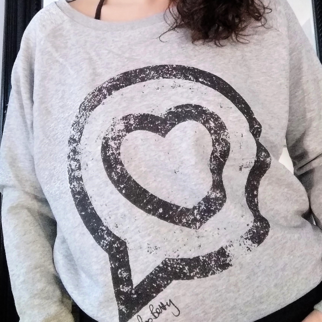 Close up of the Roo Betty Grey Ambassador Sweatshirt of the Roo betty logo of a heart in a speech bubble printed in a vintage style 